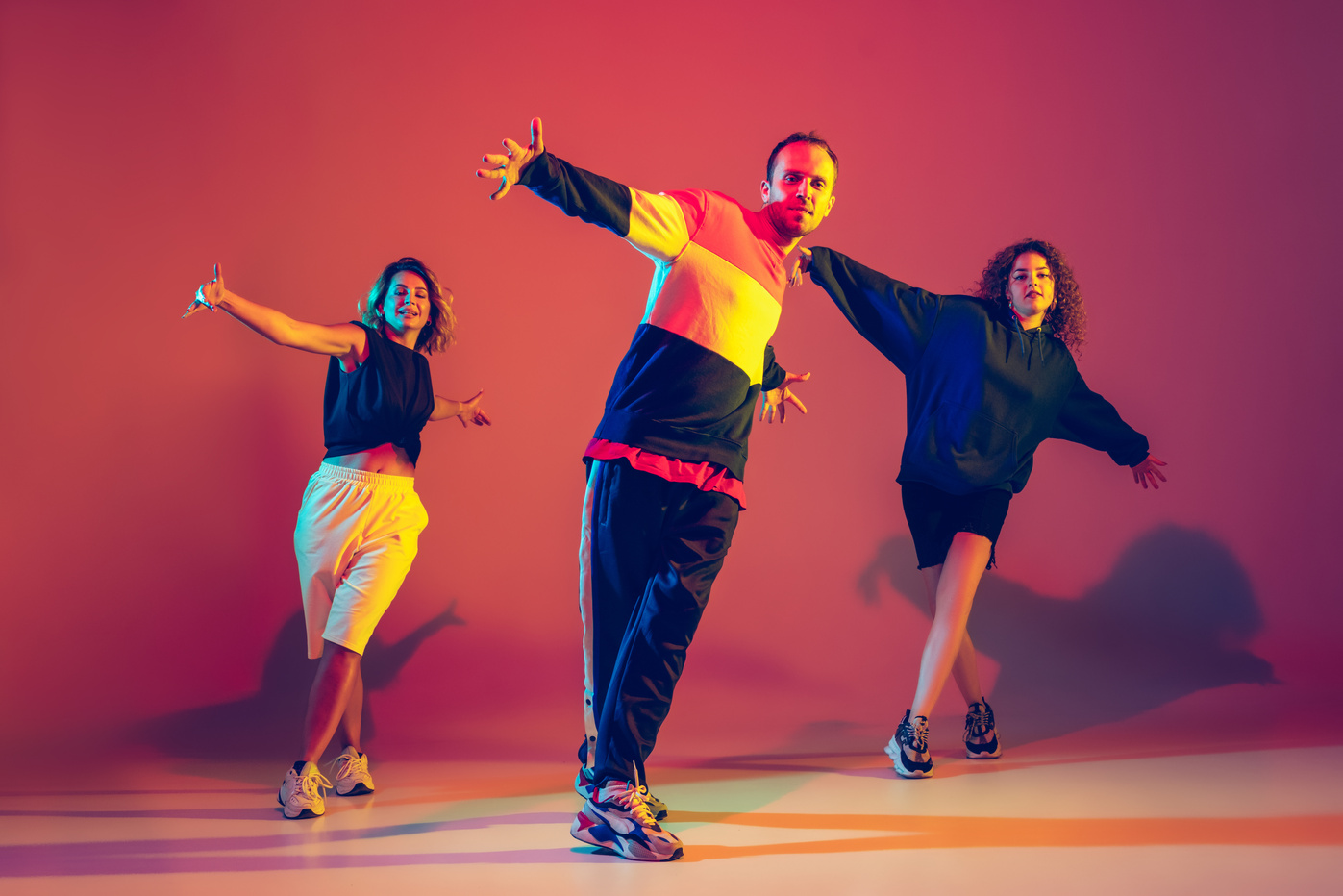 Stylish man and women dancing hip-hop in bright clothes on gradient background at dance hall in neon light